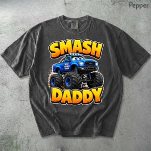 Może przedstawiać: Ciemnoszara koszulka z niebieską grafiką monster trucka i napisem "SMASH DADDY" w kolorze ż&oacute;łtym i pomarańczowym. Na ciężar&oacute;wce widnieje napis "BEST FATHER EVER". Koszulka wykonana jest z miękkiego, wygodnego materiału.