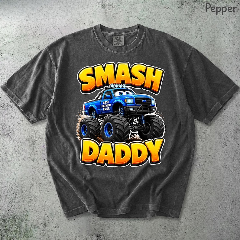 Może przedstawiać: Ciemnoszara koszulka z niebieską grafiką monster trucka i napisem "SMASH DADDY" w kolorze ż&oacute;łtym i pomarańczowym. Na ciężar&oacute;wce widnieje napis "BEST FATHER EVER". Koszulka wykonana jest z miękkiego, wygodnego materiału.