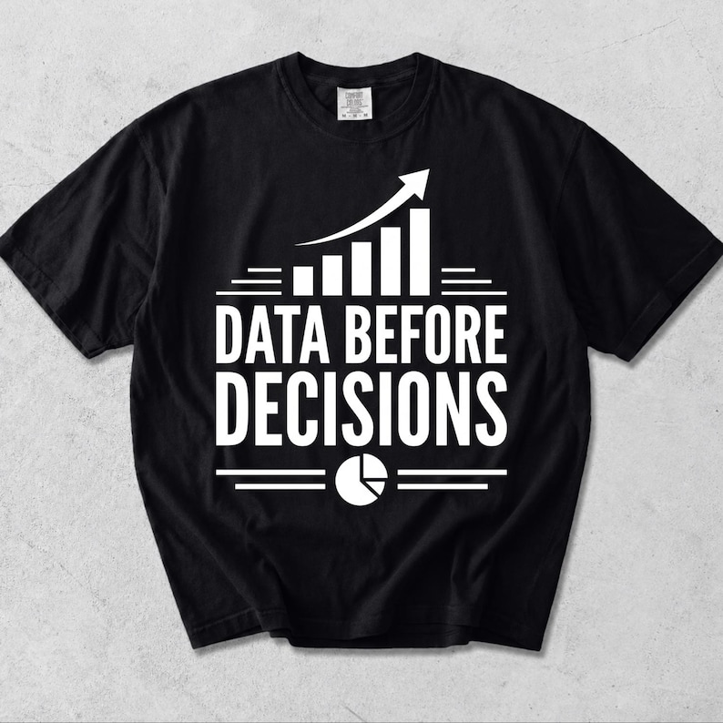 K&ouml;nnte beinhalten: Ein schwarzes Kurzarm-T-Shirt mit wei&szlig;em Grafikdruck. Das Design zeigt ein Balkendiagramm mit einem nach oben gerichteten Pfeil, den Text "DATA BEFORE DECISIONS" in fetten Gro&szlig;buchstaben und ein kreisf&ouml;rmiges Tortendiagramm-Symbol.