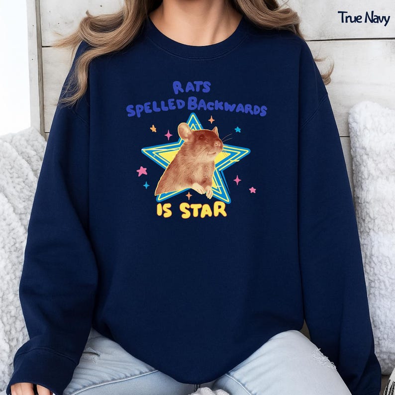 May include: True Navy sweatshirt with a graphic featuring a brown rat inside a yellow star. The text reads "Rats Spelled Backwards Is Star" in blue and white. The design includes pink and blue stars.
