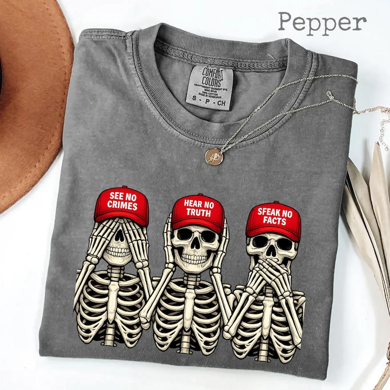May include: A gray Comfort Colors t-shirt featuring three skeleton figures in the "See No Evil, Hear No Evil, Speak No Evil" pose. Each skeleton wears a red cap with a different phrase: "See No Crimes," "Hear No Truth," and "Speak No Facts."