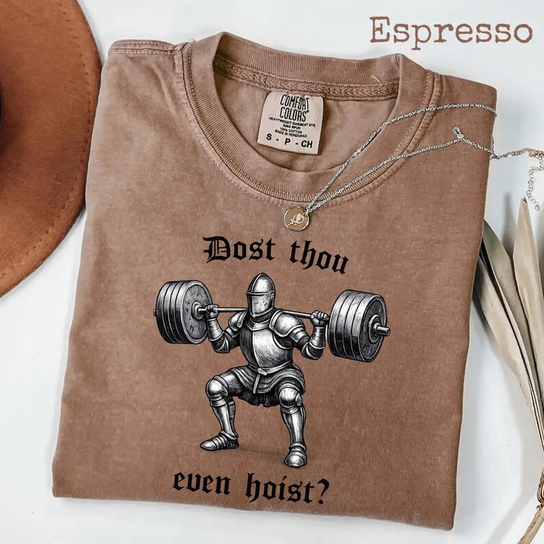 May include: Espresso-colored t-shirt with a graphic of a knight lifting weights, with the text "Dost thou even hoist?" The shirt has a Comfort Colors tag and a silver necklace. The shirt is a small size.