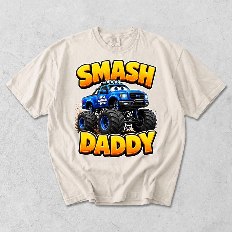Może przedstawiać: Kremowa koszulka z niebieską grafiką monster trucka i napisem "SMASH DADDY" w kolorze ż&oacute;łtym i pomarańczowym. Samoch&oacute;d ma napis "BEST FATHER EVER" z boku.