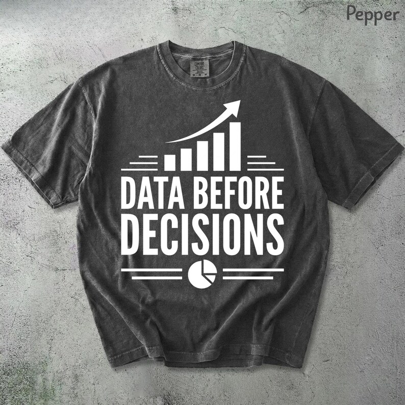 K&ouml;nnte beinhalten: Ein anthrazitfarbenes Kurzarm-T-Shirt mit wei&szlig;em Grafikdruck. Das Design zeigt ein nach oben gerichtetes Balkendiagramm, den Text "DATA BEFORE DECISIONS" in fetten Gro&szlig;buchstaben und ein kreisf&ouml;rmiges Tortendiagramm-Symbol unter dem Text.
