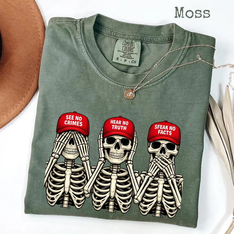 May include: Moss green t-shirt featuring three skeleton figures in the "See No Evil, Hear No Evil, Speak No Evil" pose. Each skeleton wears a red baseball cap with a different phrase: "SEE NO CRIMES", "HEAR NO TRUTH", and "SPEAK NO FACTS".