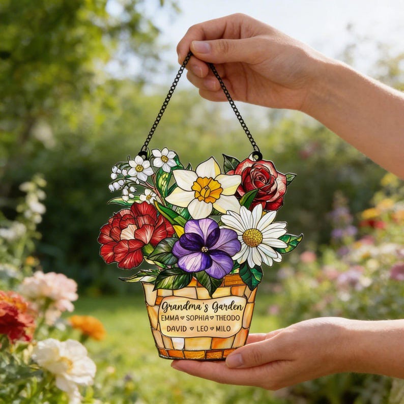 May include: A decorative garden sign featuring a bouquet of colorful flowers in a basket. The sign reads "Grandma's Garden" with names below. The sign is held by a black chain.