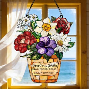May include: A hanging floral decoration featuring a bouquet of colorful flowers in a mosaic-style pot. The flowers include red roses, white daisies, and purple pansies. The text "Grandma's Garden" and names are displayed on the pot.