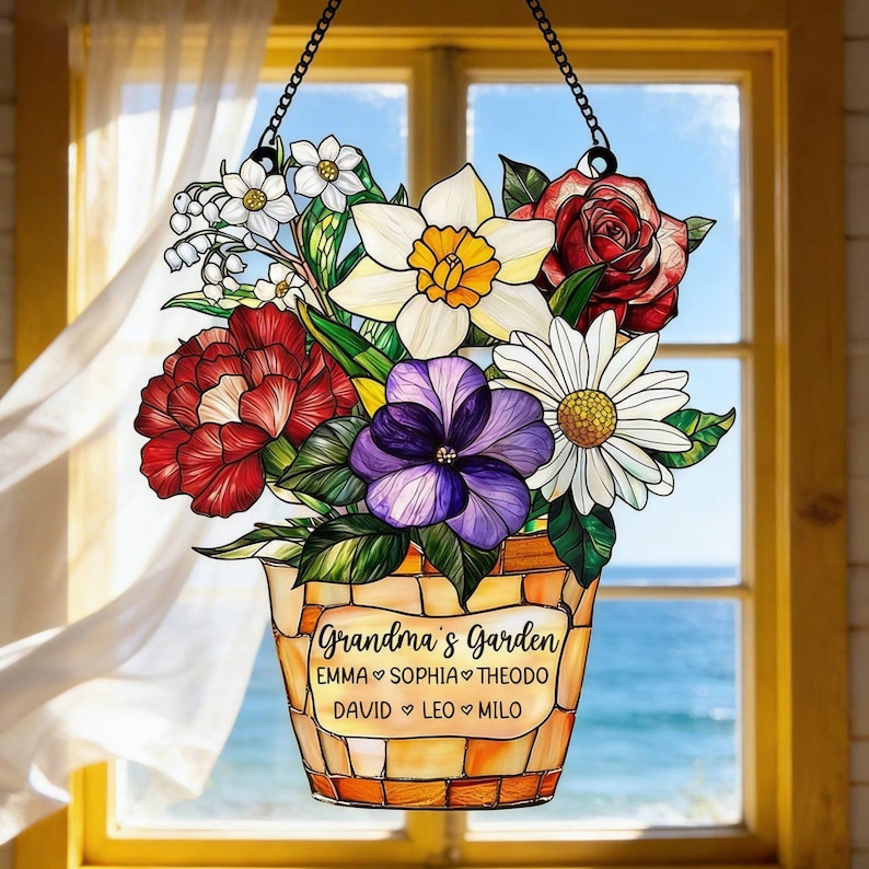 May include: A hanging floral decoration featuring a bouquet of colorful flowers in a mosaic-style pot. The flowers include red roses, white daisies, and purple pansies. The text "Grandma's Garden" and names are displayed on the pot.