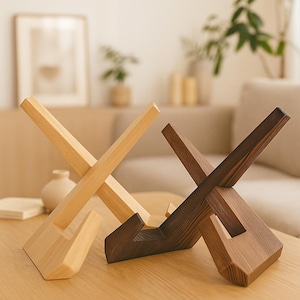May include: Two wooden book stands. One is light-coloured, the other is dark brown. Both have an X-shaped design with a base. The stands are made of wood and are designed to hold books or other items.