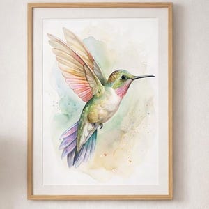 Może przedstawiać: Akwarela przedstawiająca kolibra w locie, oprawiona w jasną drewnianą ramę. Ptak ma zielone, różowe i fioletowe odcienie, ze skrzydłami w locie. Tło ma miękkie akwarelowe pociągnięcia w kolorze zielonym, żółtym i niebieskim. Grafika jest wyświetlana nad sofą.