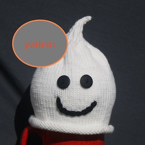 May include: White knitted ghost hat with black button eyes and a black stitched smile. The hat has a pointed top and a folded brim.