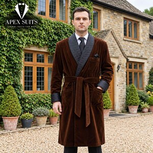 May include: A brown velvet smoking jacket featuring a black quilted shawl collar, matching quilted cuffs, a tie belt, and a chest pocket. The jacket is worn over a white collared shirt with a black necktie and a black pocket square.