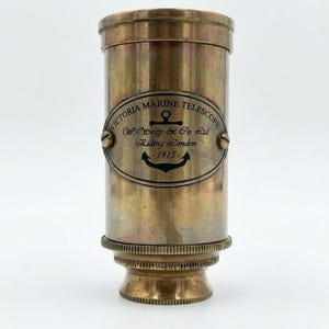 Puede incluir: Un telescopio marino Victoria de latón antiguo. Presenta una placa ovalada con el texto "Victoria Marine Telescope, W. Stacey & Co. Ltd, Riding London, 1915" y un símbolo de ancla. La base tiene un diseño decorativo y estriado.