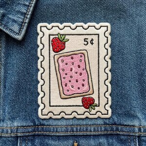 May include: A rectangular embroidered patch shaped like a postage stamp with a cream background and scalloped edges. It features a central pink frosted pastry with red sprinkles, two red strawberries, and the black text 5 cents printed on it.