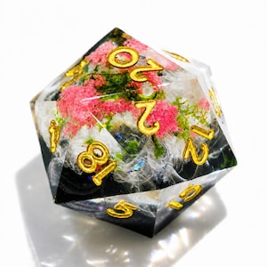 Könnte beinhalten: Ein zwanzigseitiger Würfel mit floralem Design. Der transparente Harzwürfel zeigt rosa und weiße Blumen mit goldfarbenen Zahlen. Die Basis des Würfels ist schwarz, und die Blumen sind in dem transparenten Harz eingeschlossen.