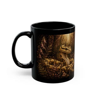 May include: Black ceramic mug featuring a detailed illustration of a snake wearing a crown, set in a forest scene. The snake has a yellow and brown pattern. The mug has a curved handle.