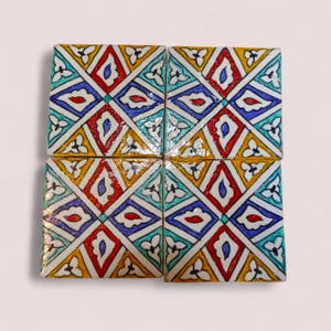 Könnte beinhalten: Vier quadratische Keramikfliesen mit einem farbenfrohen geometrischen Design. Jede Fliese weist ein sich wiederholendes Muster aus Rauten, Tropfen und floralen Elementen in Rot, Blau, Gelb und Weiß auf. Die Fliesen sind quadratisch angeordnet.