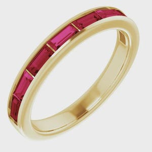 Könnte beinhalten: Ein goldener Bandring mit einer Reihe rechteckiger, leuchtend roter Edelsteine. Das Design zeigt eine durchgehende Reihe roter Steine, die in das Goldband eingesetzt sind und einen auffälligen Kontrast erzeugen. Der Ring ist ein Schmuckstück.
