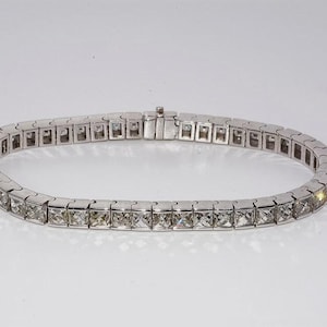 Può includere: Un bracciale d'argento con pietre preziose a taglio quadrato. Il bracciale, di forma ovale, ha una chiusura. Le pietre preziose, chiare, riflettono la luce, creando un effetto scintillante. Un gioiello.