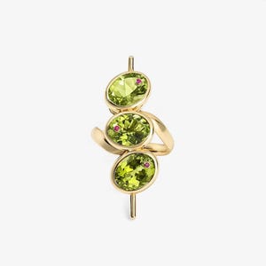 May include: A gold ring featuring three oval-cut peridot gemstones, each accented with a small, round ruby. The peridots are a vibrant green, set in a gold band. The ring has a unique, vertical design.