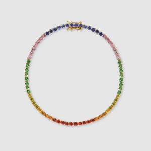 May include: A gold-toned necklace featuring a rainbow of gemstones. The gemstones transition from red to orange, yellow, green, pink, and blue. The necklace has a clasp closure.