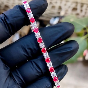 Puede incluir: Una pulsera de tenis plateada con piedras preciosas rojas y claras alternadas. El diseño de la pulsera presenta piedras de talla redonda y espaciadas uniformemente. Las piedras rojas se intercalan con piedras claras y brillantes.