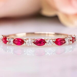 May include: A delicate ring featuring alternating marquise-cut red gemstones and round, clear gemstones set in a gold band. The ring's design is symmetrical, with the gemstones evenly spaced around the band.