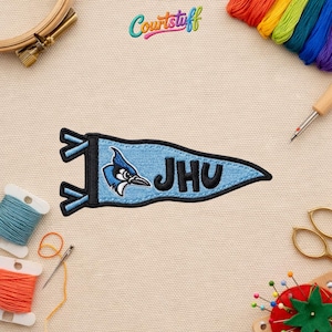 May include: A light blue pennant-shaped patch with the text "JHU" and a blue jay mascot. The patch is outlined in black and has a black border. The word "Courtstuff" is written in colorful letters at the top.