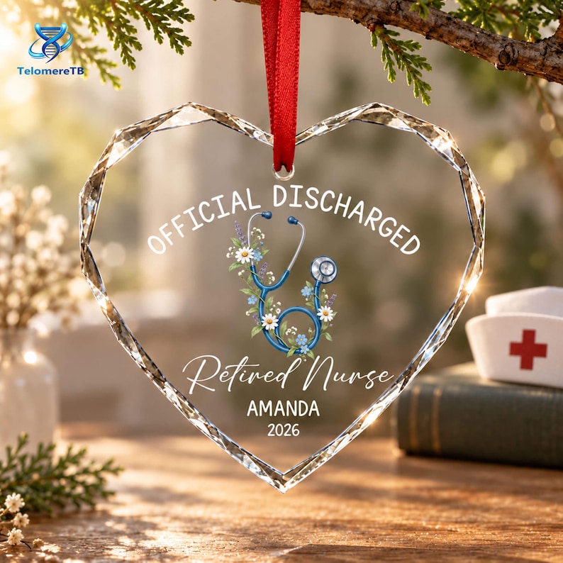 May include: A heart-shaped clear acrylic ornament with faceted edges, suspended by a red ribbon. It features a blue stethoscope graphic surrounded by small flowers, with the text OFFICIAL DISCHARGED, Retired Nurse, AMANDA, and 2026 printed in white.