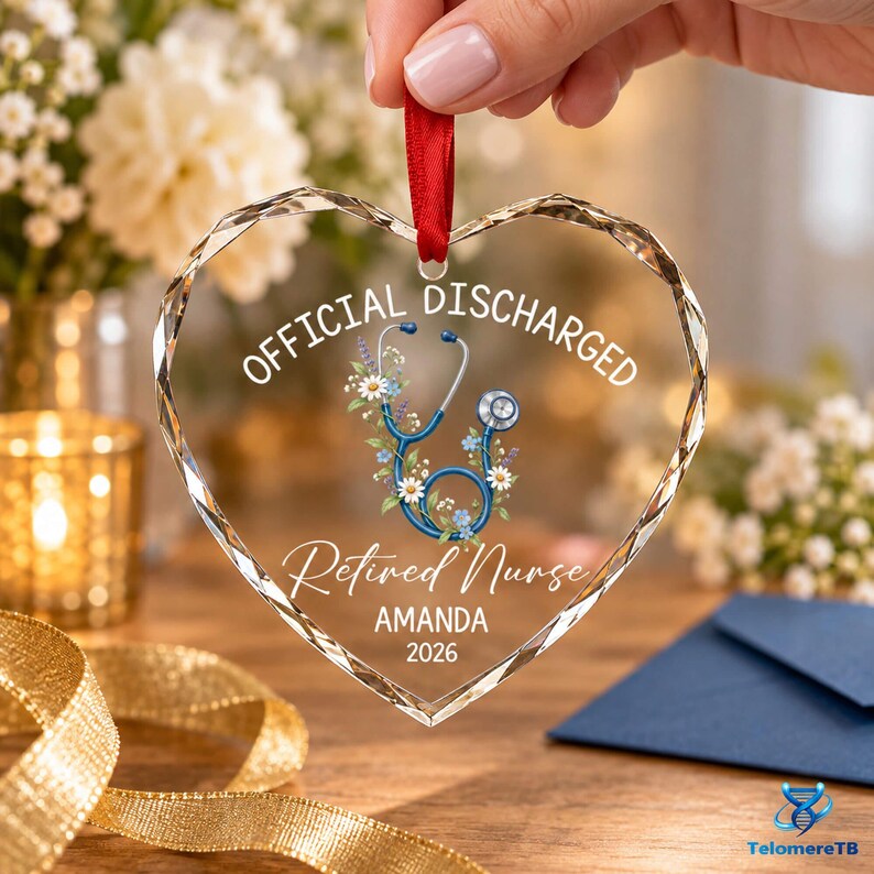 May include: A heart-shaped clear acrylic ornament with a red ribbon hanger. The text reads OFFICIAL DISCHARGED, Retired Nurse, AMANDA, and 2026. A blue stethoscope graphic is intertwined with white and purple flowers in the center of the ornament.