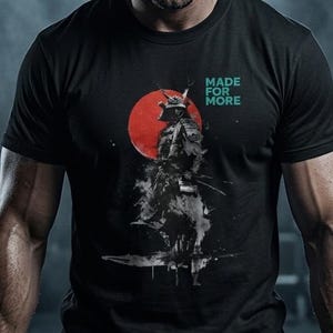 以下が含まれることがあります： 黒いTシャツ。赤い太陽を背景に侍のグラフィック、ターコイズ色の「MADE FOR MORE」の文字。ジムでバーベルを持ち上げる人の画像。