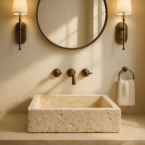 Peut inclure: Une salle de bain avec un lavabo en pierre rectangulaire, un miroir rond et des appliques murales. La robinetterie est en bronze, et une serviette blanche est suspendue à un anneau assorti. L'ambiance est chaleureuse.
