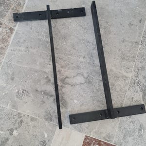 May include: Two black metal shelf brackets. Each bracket has a horizontal base with pre-drilled holes and a vertical support. The brackets are designed for wall mounting and are suitable for supporting shelves or other items.