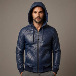 Può includere: Una giacca con cappuccio in pelle blu navy caratterizzata da una texture che ricorda la pelle di struzzo, una cerniera frontale a tutta lunghezza con tirante in pelle abbinato, maniche lunghe con polsini a coste e cappuccio con coulisse metallica.