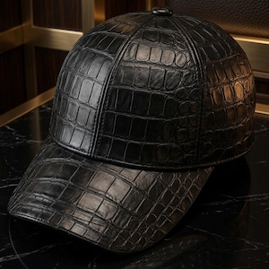 Könnte beinhalten: Eine schwarze Baseballkappe mit einer strukturierten Krokodilleder-Optik auf der gesamten Oberfläche. Die Kappe verfügt über eine strukturierte Krone mit einem zentralen Knopf an der Oberseite und einen gebogenen Schirm mit glänzendem Finish.