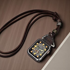 May include: A silver smartwatch pendant with a brown leather strap. The watch face displays a detailed design with yellow and white accents. The pendant hangs from a long, dark brown leather cord.