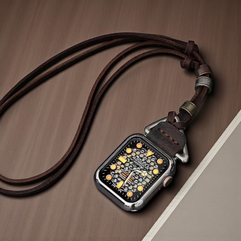 May include: A silver smartwatch pendant with a brown leather strap. The watch face displays a detailed design with yellow and white accents. The pendant hangs from a long, dark brown leather cord.