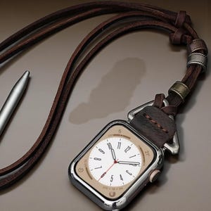 May include: A silver smartwatch with a cream-colored face and black numerals is attached to a brown leather strap. The strap is designed to be worn around the neck. A silver stylus is also visible.