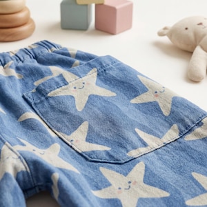 Close-up of handmade kids barrel pants in blue cotton fabric with star print, showing large front patch pocket and elastic waistband detail