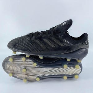 May include: Black Adidas Copa football boots with a textured leather upper and a rubber sole. The boots have a lace-up closure and the Adidas logo on the tongue. The word "COPA" is printed on the side.