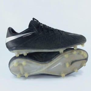 Könnte beinhalten: Schwarze Fußballschuhe mit strukturiertem Obermaterial und weißem Nike-Swoosh. Die Schuhe haben ein flaches Design mit transparenten Stollen an der Sohle. Das Wort "HYPERVENOM" ist auf der Seite aufgedruckt.