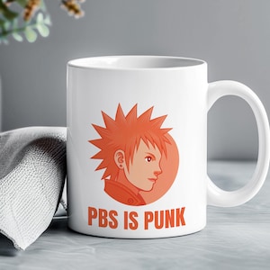 May include: White ceramic mug with an orange cartoon character with spiky hair and the text "PBS IS PUNK". The character is set against an orange circle. The mug has a curved handle.