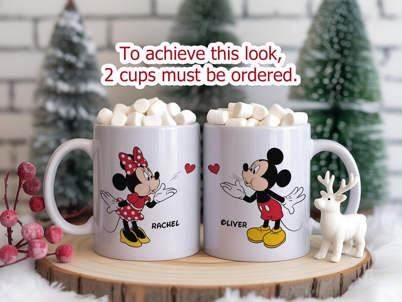 K&ouml;nnte beinhalten: Zwei wei&szlig;e Keramikbecher gef&uuml;llt mit Marshmallows, mit Minnie- und Mickey-Mouse-Designs. Auf einem Becher steht "Rachel" und auf dem anderen "Oliver". Der Text "To achieve this look, 2 cups must be ordered" ist ebenfalls sichtbar.