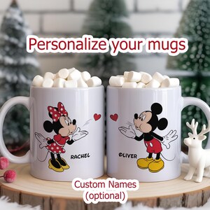 Two white mugs filled with marshmallows, featuring Mickey and Minnie Mouse designs. Each mug has a name printed on it. The text "Personalize your mugs" is at the top. The words "Custom Names (optional)" are at the bottom.