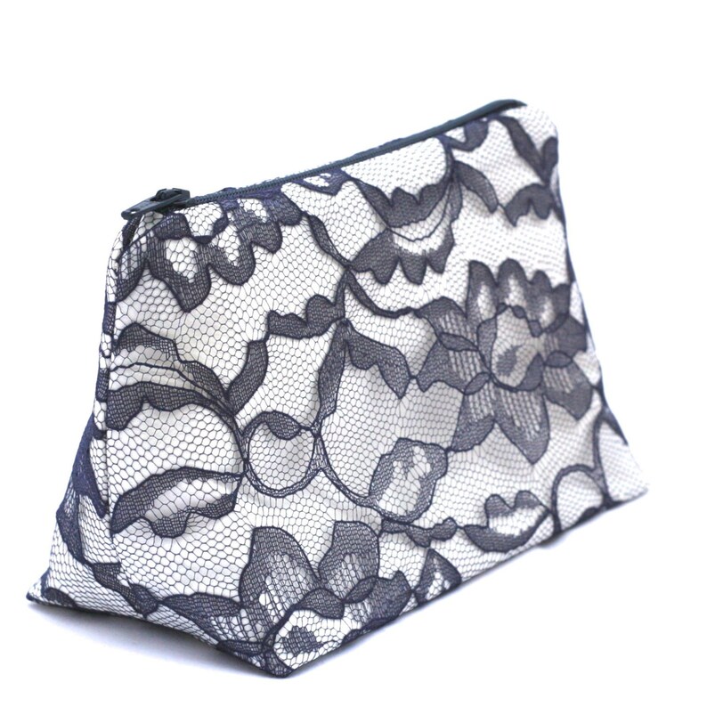 May include: A black and white lace cosmetic bag with a zipper closure. The bag is made of a soft, delicate fabric and has a floral pattern.