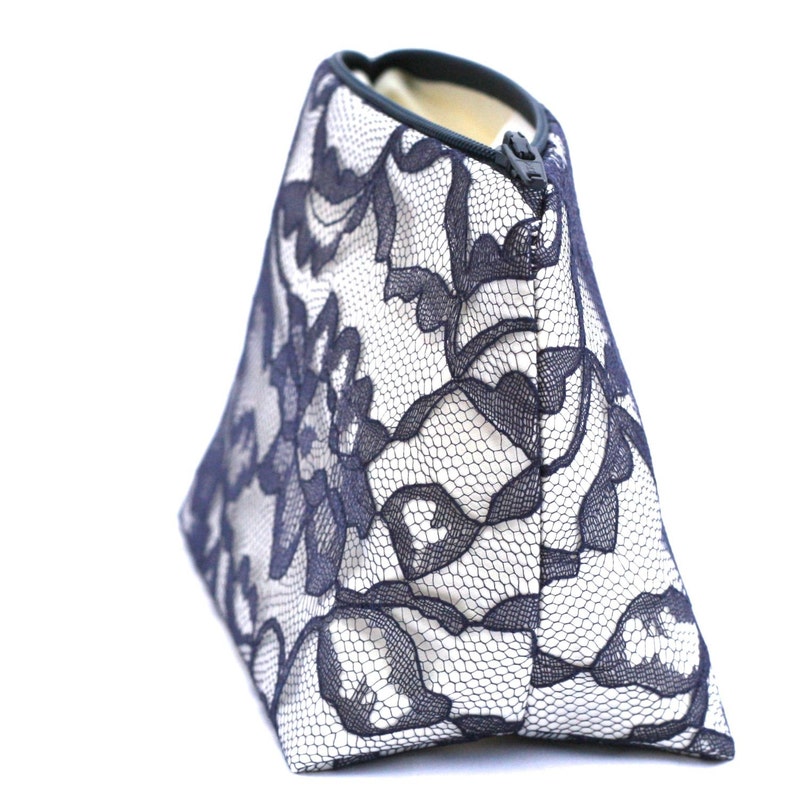 May include: A white zippered pouch with a black lace pattern. The pouch is made of fabric and has a zipper closure.