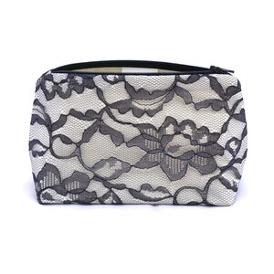 May include: A white zippered pouch with a black lace pattern.