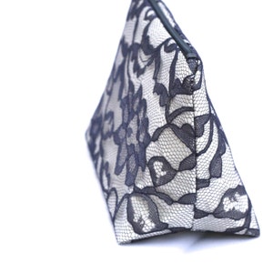 May include: A white and black lace cosmetic bag with a zipper closure. The bag is triangular in shape and has a floral pattern.