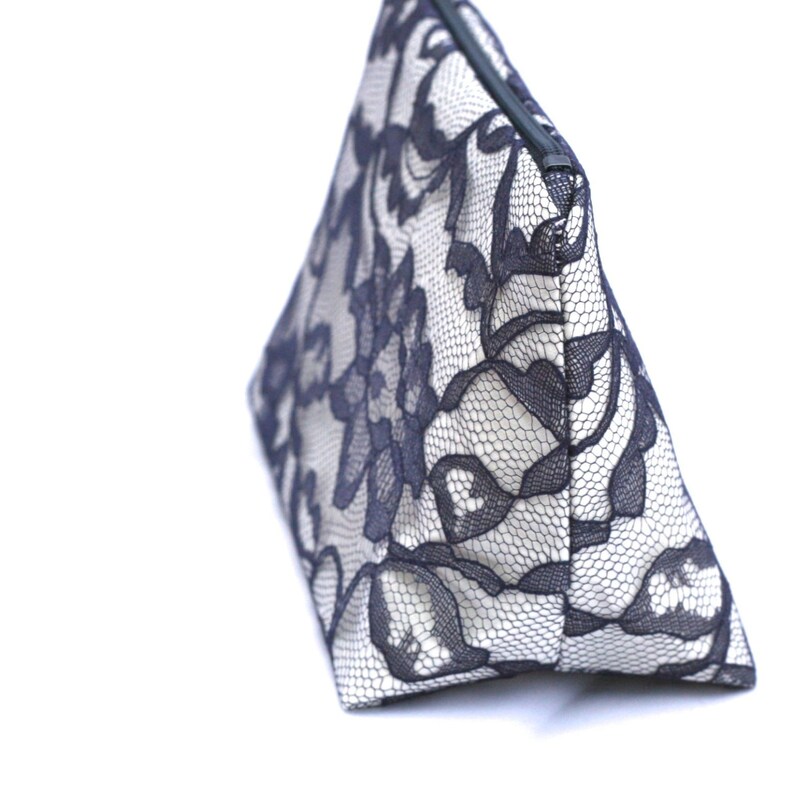 May include: A white and black lace cosmetic bag with a zipper closure. The bag is triangular in shape and has a floral pattern.