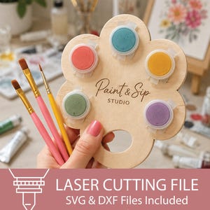 Pode incluir: Uma paleta de pintura de madeira clara em forma de flor com cinco recortes circulares contendo pequenos potes de tinta nas cores coral, azul-petróleo, amarelo, verde e roxo. O texto Paint & Sip STUDIO está gravado no centro da peça.